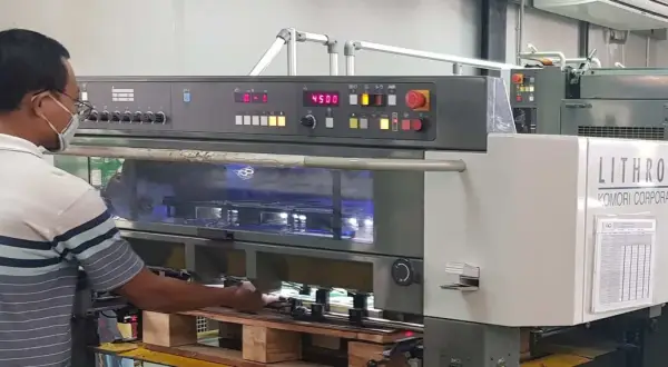 Operator w maszynie drukarskiej Komori Lithrone A37 z panelem sterowania i wyświetlaczem.
