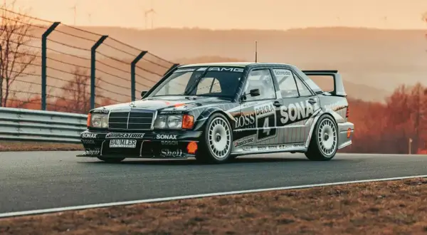 Czarny Mercedes 190 Evo na torze wyścigowym, z licznymi sponsorami na karoserii, gotowy do startu.