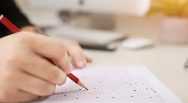 Dłoń z ołówkiem zaznacza odpowiedzi na arkuszu. Zastanawiasz się, ile trzeba mieć procent z egzaminu zawodowego żeby zdać?