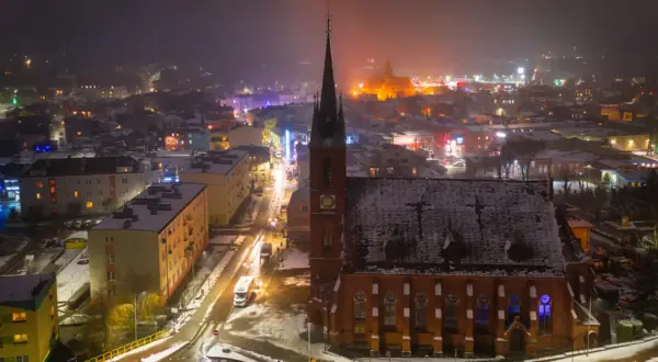 Nocna panorama Kościerzyny, ośnieżona trasa miejska z kościołem w centrum i rozświetlonymi budynkami.