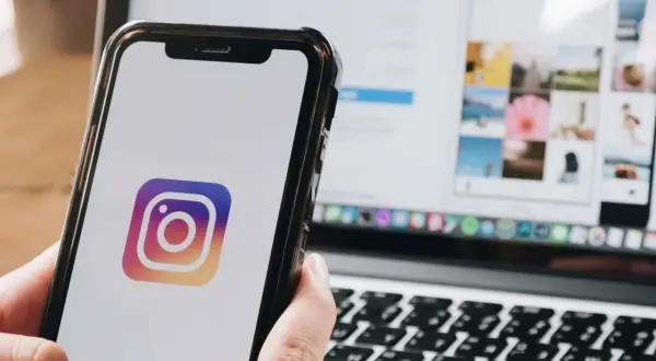 Telefon z logo Instagram. Na ekranie laptopa widać siatkę zdjęć, jakbyś chciał dowiedzieć się, jak wstawić czyjąś relację na swoją.