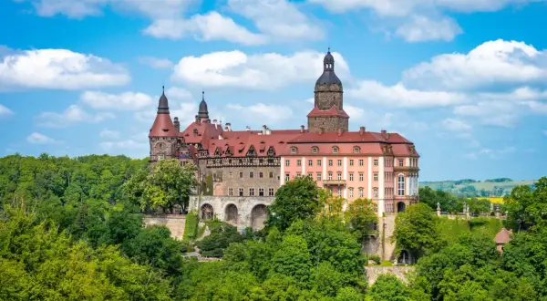 Imponujące pałace w Polsce, jak ten z czerwonym dachem i wieżami, otoczone bujną zielenią, kuszą historią i baśniowym klimatem.