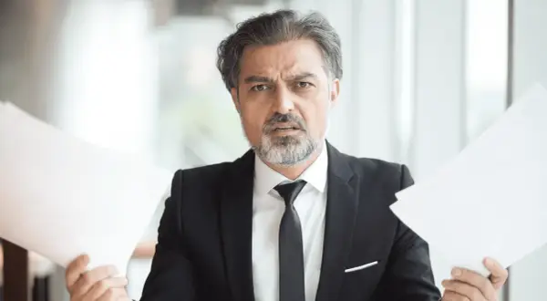 Hombre con traje y papeles, preocupado por cuanto cobra una inmobiliaria por alquilar un piso.