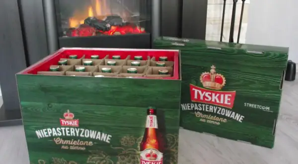 Dwie zielone skrzynki piwa Tyskie Niepasteryzowane Chmielone na zimno stoją obok siebie. W jednej widać rzędy butelek.