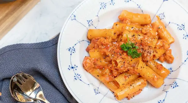 En tallrik med krämig pasta alla zozzona, toppad med persilja och svartpeppar. Bredvid ligger en servett och bestick.