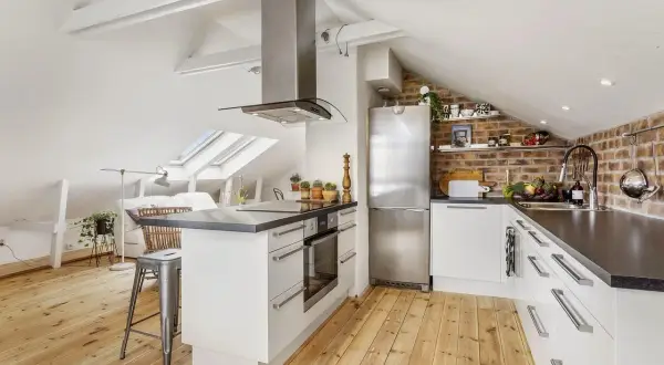 Accogliente cucina in mansarda bassa con soffitto spiovente, elettrodomestici in acciaio e mattoni a vista.