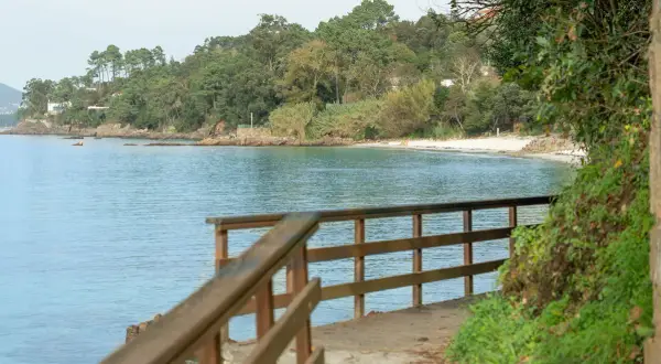 Camino de madera hacia la playa Mogor, con el mar azul y la costa verde al fondo.