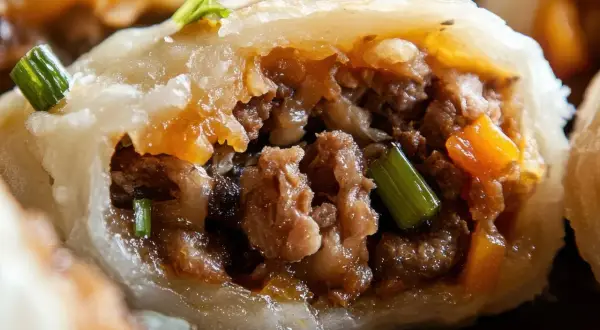 Pyszne pierogi z mięsem, z widocznym farszem i zieloną cebulką, kuszą apetycznym wyglądem.