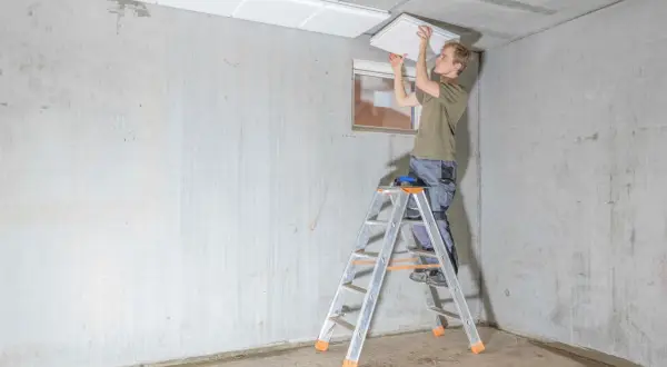 Mann montiert weiße Platten an der Kellerdecke zur Isolierung.