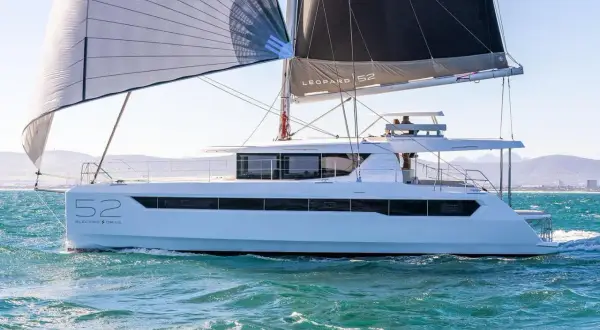 Un catamarano Leopard 52 con vele spiegate naviga su acque turchesi, con montagne sullo sfondo.