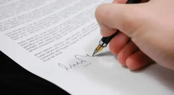 Dłoń podpisuje dokument, być może oświadczenie o odrzucenie spadku.