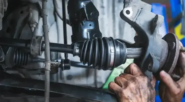 Mechanik sprawdza przegub zewnętrzny w samochodzie. Widać gumową osłonę i metalowe elementy.