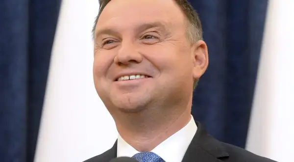 Uśmiechnięty Andrzej Duda, jego wiek nie jest widoczny na zdjęciu, ale wygląda na dojrzałego mężczyznę w garniturze.