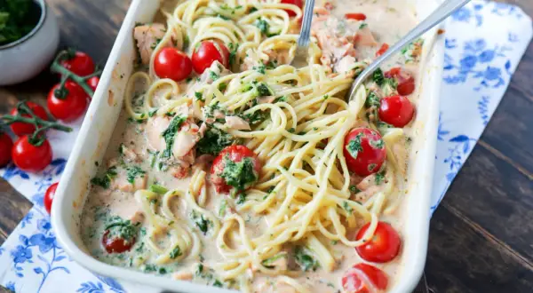 Herzhafte Lachs Spinat Pasta in cremiger Sauce mit Kirschtomaten, serviert in einer Auflaufform.