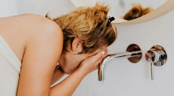 Femme se lavant le visage, soulagée de ne pas avoir d'allergie à l'eau calcaire.