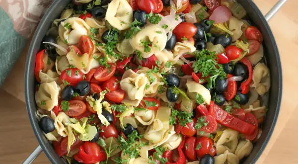 Kolorowa sałatka z tortellini, pomidorkami koktajlowymi, czarnymi oliwkami, papryką i natką pietruszki w patelni.