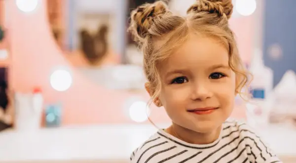 Urocza dziewczynka z blond włosami upiętymi w dwa kucyki. Jej fryzura to idealne włosy dla dziewczyn, które chcą wyglądać modnie i dziewczęco.