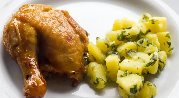 Pieczone udko kurczaka z ziemniakami i natką pietruszki na białym talerzu.