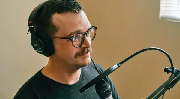 Mężczyzna w okularach i słuchawkach przygotowuje się do nagrywania mikrofonu.