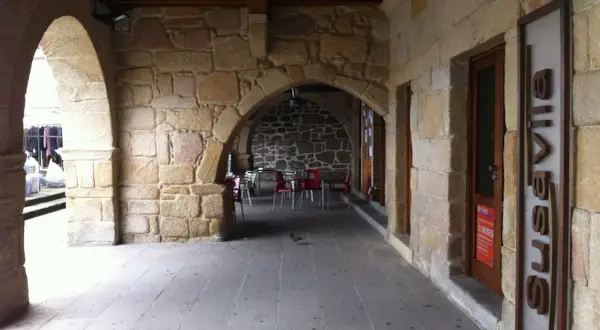 Arcadas de piedra en el casco antiguo de Galicia, con mesas y sillas de exterior. Los muros de piedra transmiten la historia de la zona.