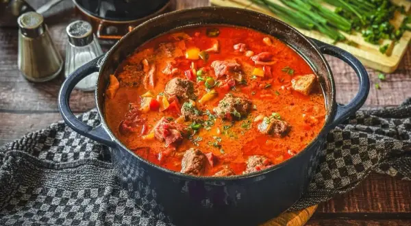 Herzhaftes Pfundstopf Rezept in einem Gusseisentopf, mit Fleischklößchen, Paprika und einer würzigen Tomatensoße, garniert mit frischen Kräutern.