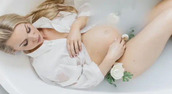 Kobieta w białej koszuli w wannie z kwiatami. Piękna sesja ciążowa, w którym tygodniu?