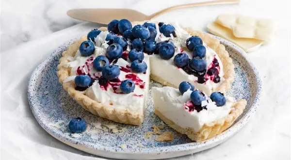 Tarta z kremem z białej czekolady, udekorowana borówkami i wiórkami białej czekolady. Wygląda pysznie!