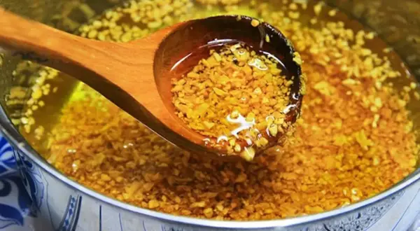 Holzschöpfkelle hebt goldbraun angebratenen Knoblauch aus heißem Öl. Knoblauch anbraten oder nicht? Hier die Antwort!