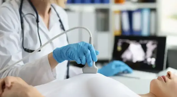 Lekarka wykonuje badanie USG piersi, sprawdzając znamiona. Na ekranie komputera widoczny obraz.