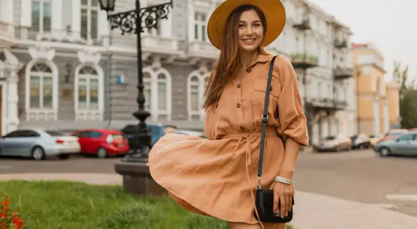 Uśmiechnięta kobieta w beżowej sukience i kapeluszu, rozmiar 42, spaceruje po mieście.