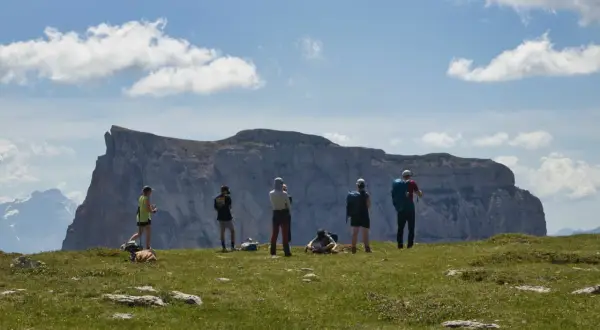Groupe de randonneurs admirant un impressionnant plateau rocheux lors d'un trek dans le Vercors. Ciel bleu et nuages blancs.