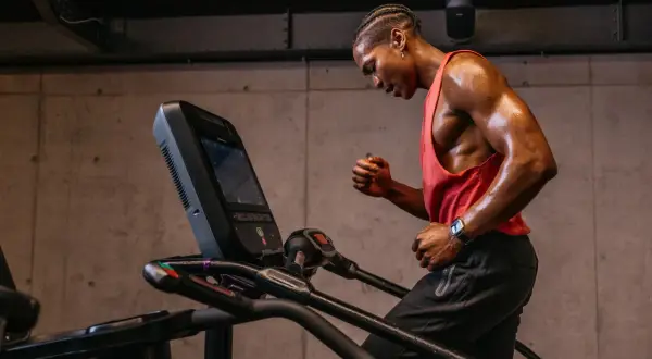Schweißglänzender Mann im roten Tanktop gibt alles beim liss cardio auf dem Laufband.