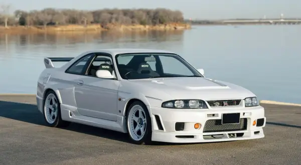 Białe r33 GT-R z siedzeniami Nismo stoi nad jeziorem.