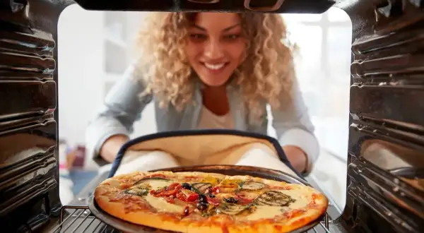 Kobieta wyjmuje z piekarnika pyszną pizzę. Idealna temperatura do pieczenia pizzy to klucz do sukcesu.