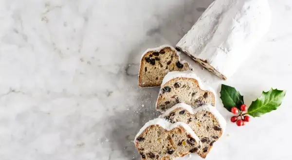 Le stollen, un délice de Noël, est saupoudré de sucre glace. Des tranches révèlent des fruits secs et des baies rouges sur une branche de houx.