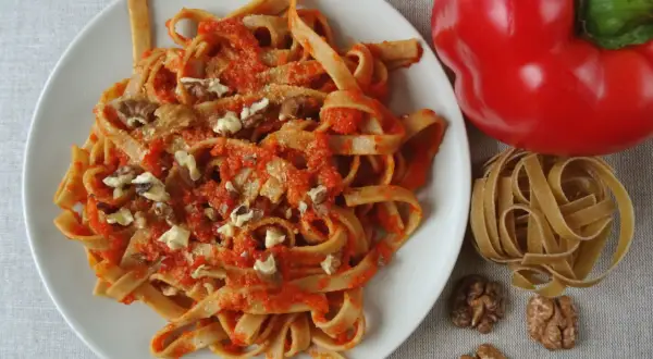 Pyszne spaghetti z papryką i orzechami włoskimi, obok czerwona papryka i surowy makaron.