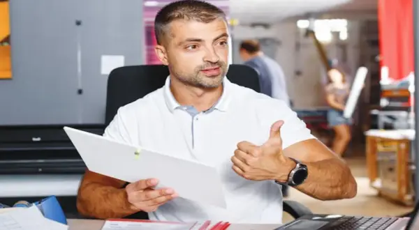 Mężczyzna w białej koszulce trzyma dokument i pokazuje kciuk w górę.