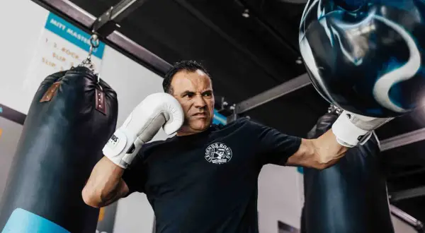 Man with intense focus, performing boxing workouts at home with a heavy bag. He wears white gloves and a black t-shirt.