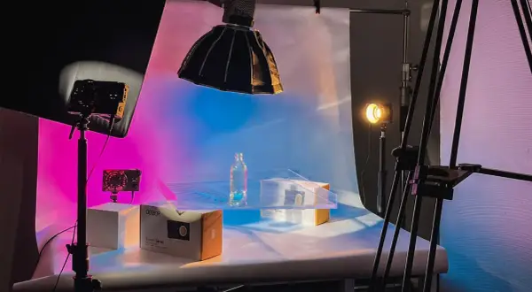Product photography setup with a bottle and boxes on a table, illuminated by colorful background light and studio lights.