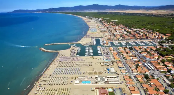 Vista aerea di una località balneare in provincia di Grosseto, con spiaggia attrezzata, porto turistico e case con tetti rossi.