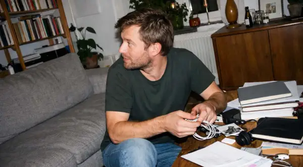 Man med skägg sitter vid ett skrivbord med papper och böcker. Han jobbar hemifrån med sitt eget uttag som enskild firma.