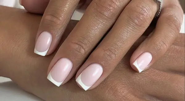 Delikatny french manicure z różowymi paznokciami, jak płatki kwiatów. Na serdecznym palcu błyszczący pierścionek.