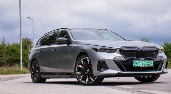 Srebrne BMW i5 na tle pochmurnego nieba, z widocznymi felgami i tablicą rejestracyjną.