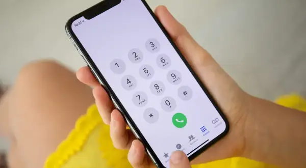 Dłoń trzyma smartfon z klawiaturą numeryczną. Możliwość wykonywania połączeń przez Wi-Fi ułatwia kontakt.
