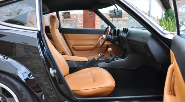 Wnętrze klasycznego Datsuna 280Z z brązową skórzaną tapicerką i drewnianą kierownicą.