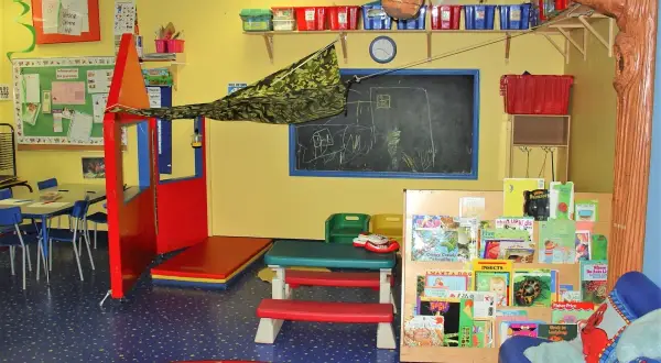 Ein farbenfroher Gruppenraum mit Spielzeug, Büchern und einer Tafel, der den Raum als dritten Erzieher für Kinder gestaltet.