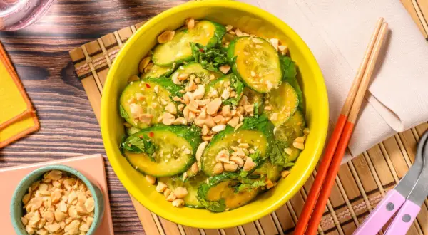 En skål med asiatisk gurksallad, toppad med hackade jordnötter och färska örter. Serveras med ätpinnar.