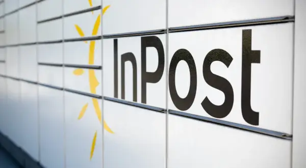 Czy do paczkomatu InPost trzeba drukować etykietę? Zbliżenie na białą obudowę paczkomatu z czarnym logo InPost i żółtym symbolem.