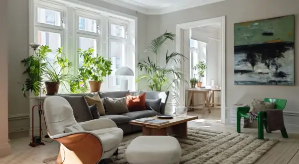 Ett vardagsrum med bohemisk inredning, fyllt med gröna växter, en bekväm soffa och en konstnärlig tavla på väggen.