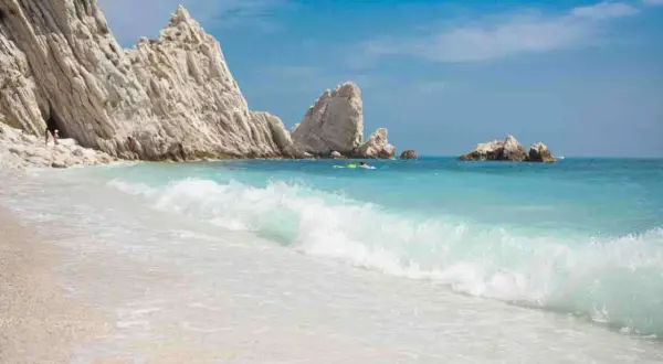 Spiaggia delle Due Sorelle: onde turchesi lambiscono la riva, rocce bianche imponenti si ergono sul mare azzurro, un paradiso incontaminato.